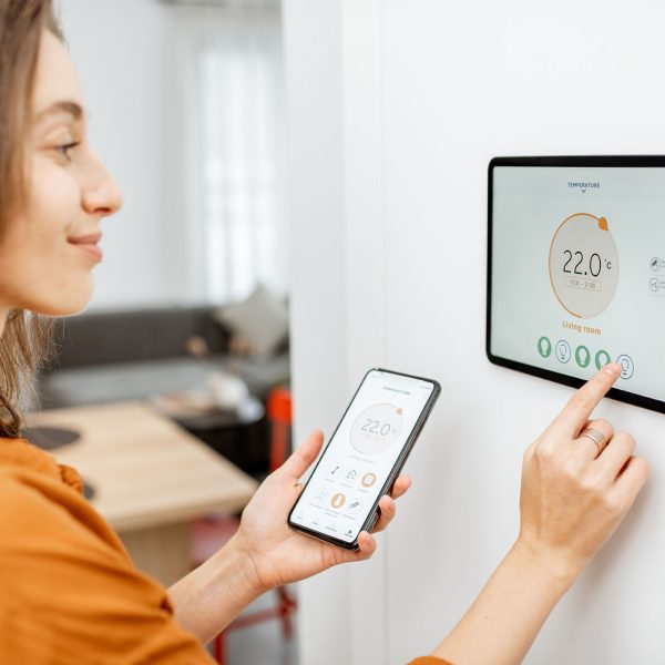 Young woman controlling temperature in the living room with smart phone and digital touch screen panel. Concept of heating control in a smart home