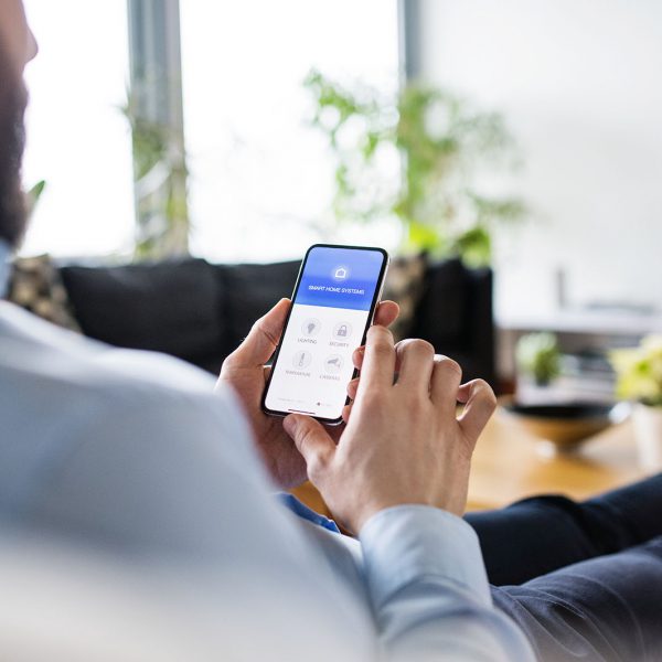 An unrecognizable man holding a smartphone with smart home control system.